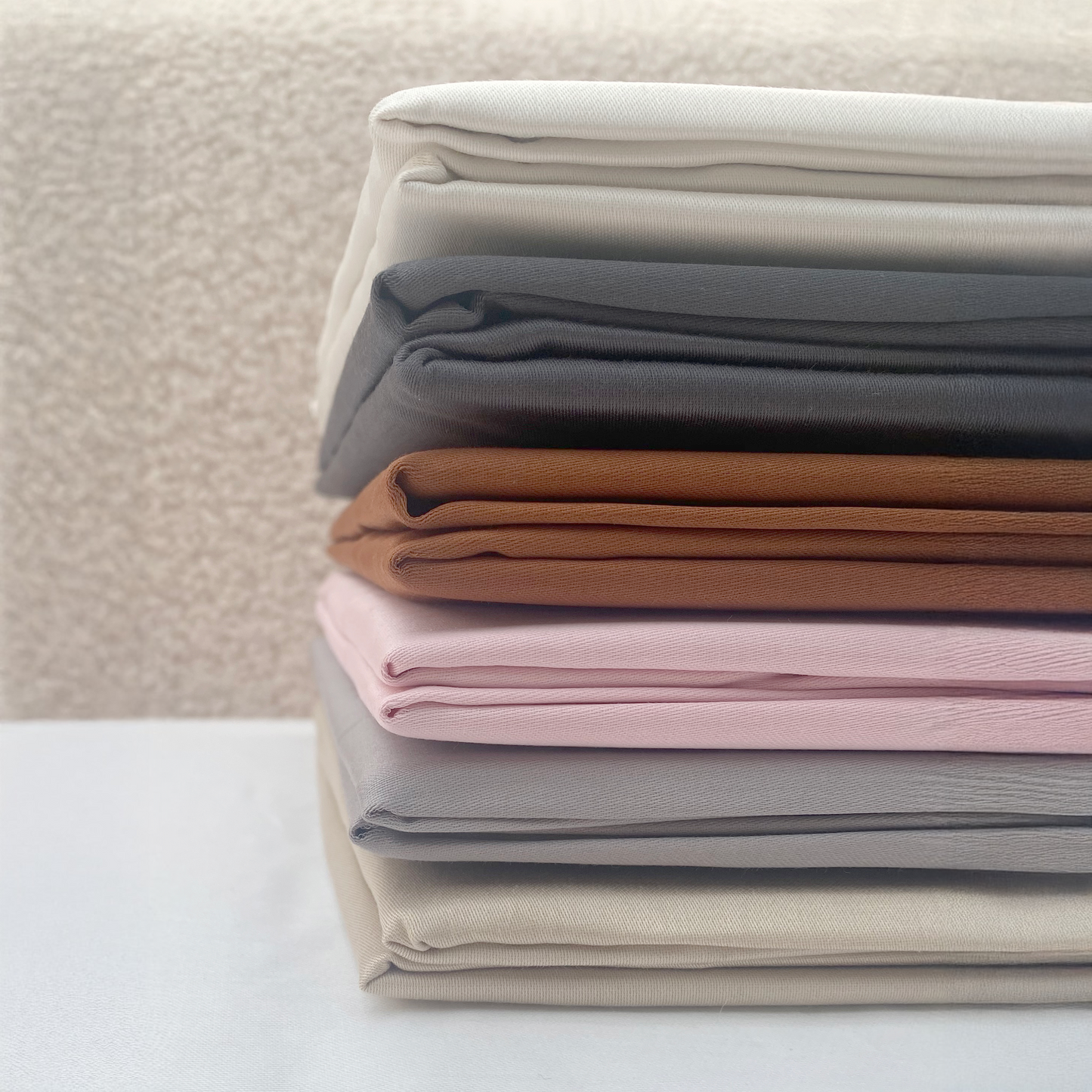 Stack of folded fabric cotton statin sheets in various colors on a neutral background