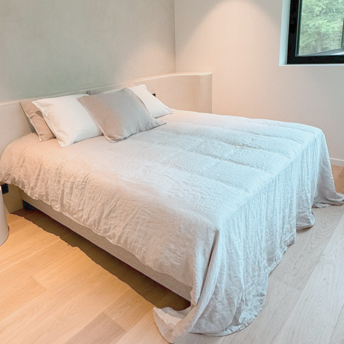 A fixed boxspring bed with a beige mattress, black fabric, and white wooden legs in a room with modern decor.