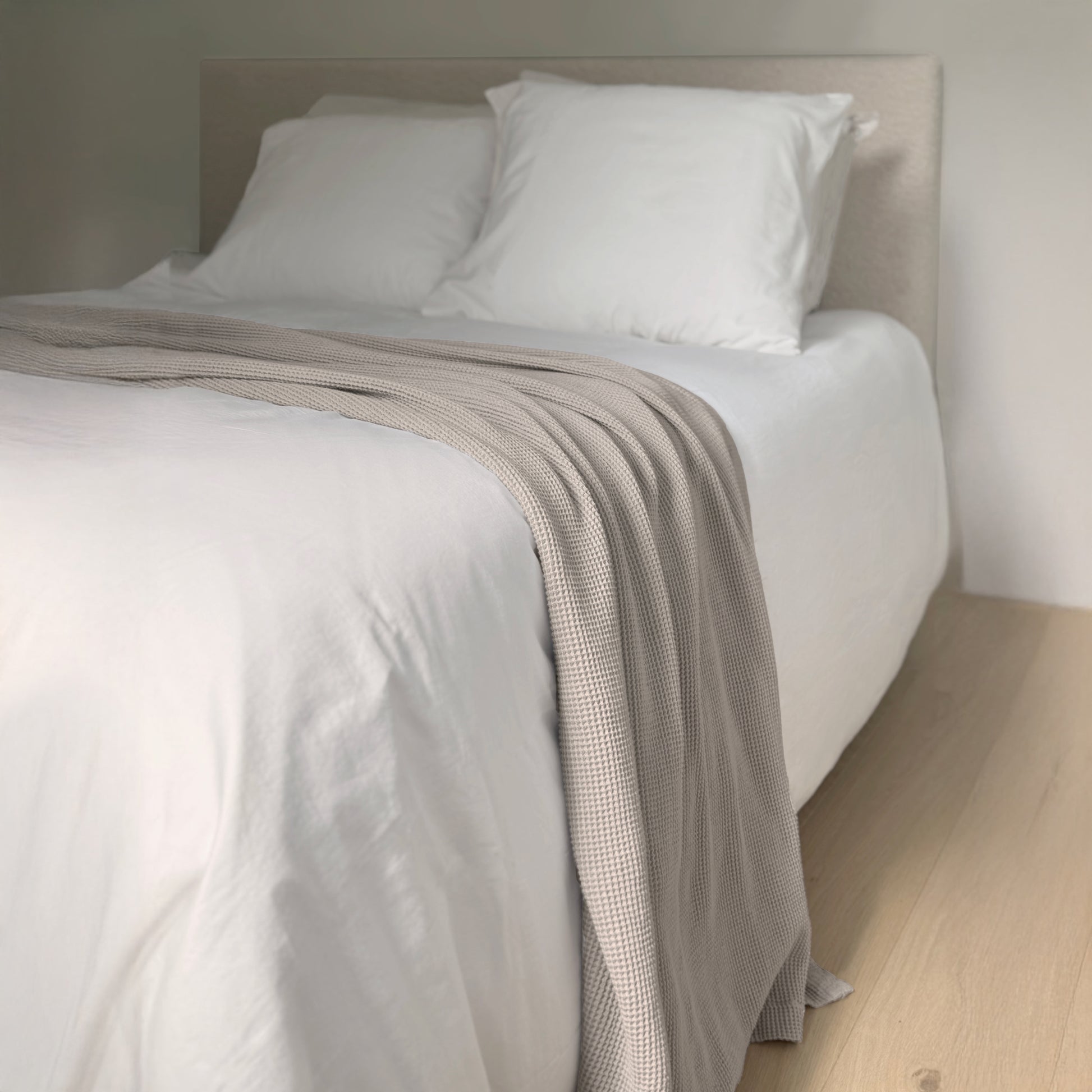Bed with white bedding and a beige blanket in a minimalistic room.