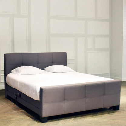 Black upholstered bed with white mattress and pillows against a white paneled wall.