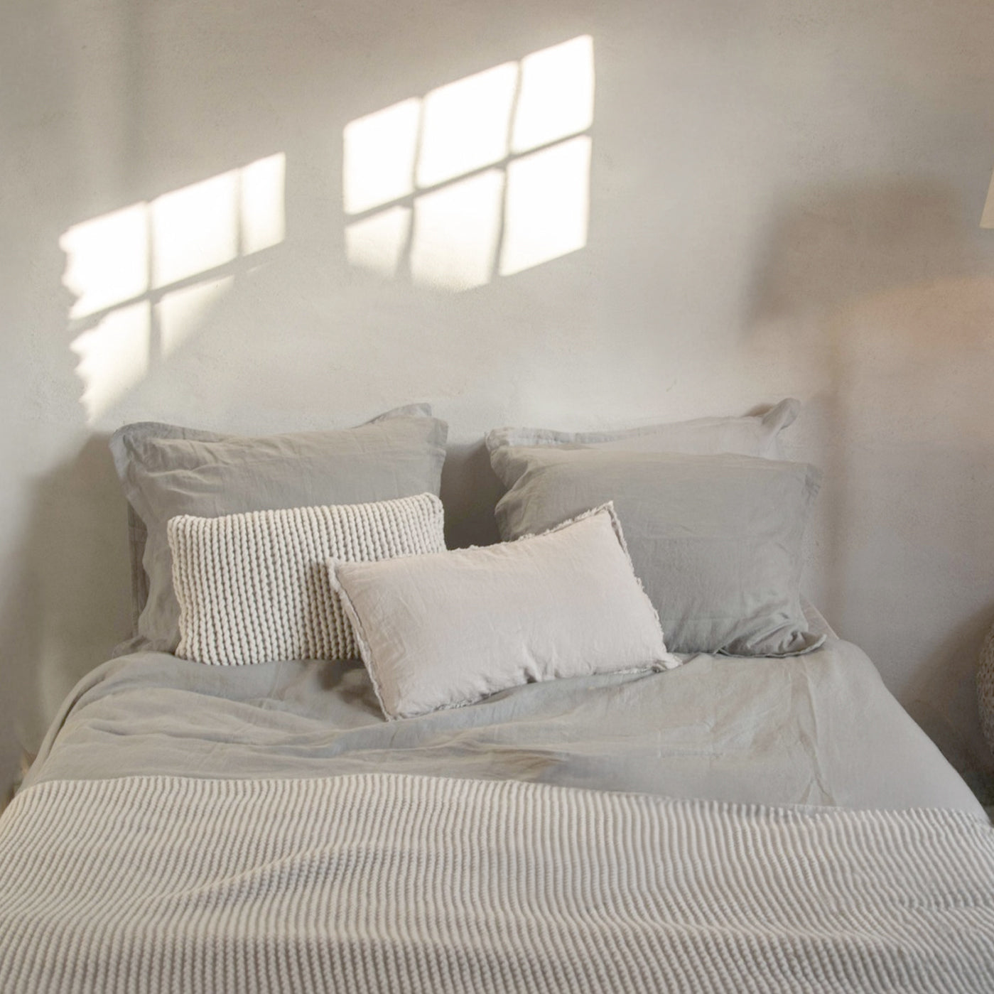 Neatly made bed with light-colored bedding and pillows in a softly lit room.
