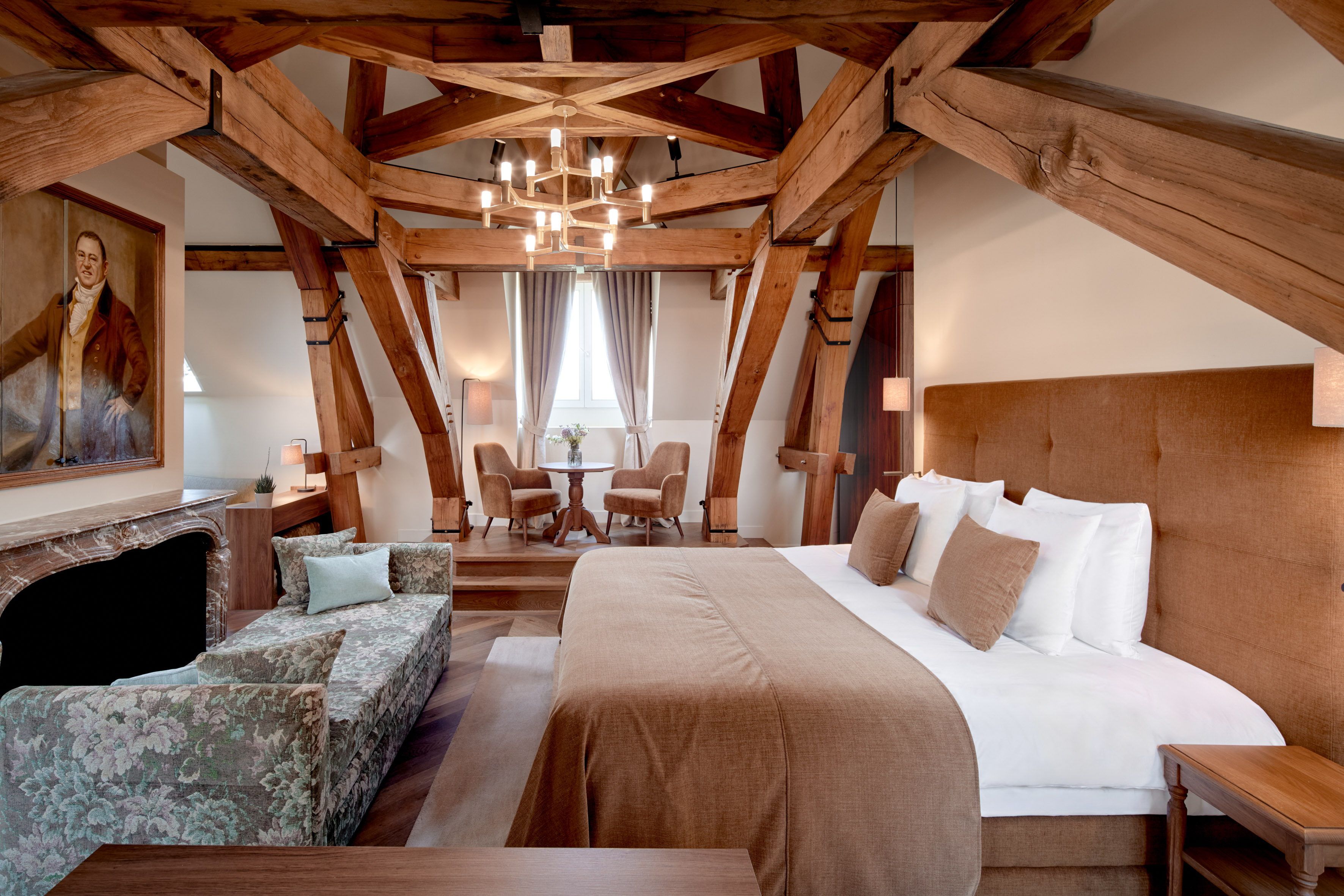 Luxurious bedroom with wooden beams, bed, and seating area.