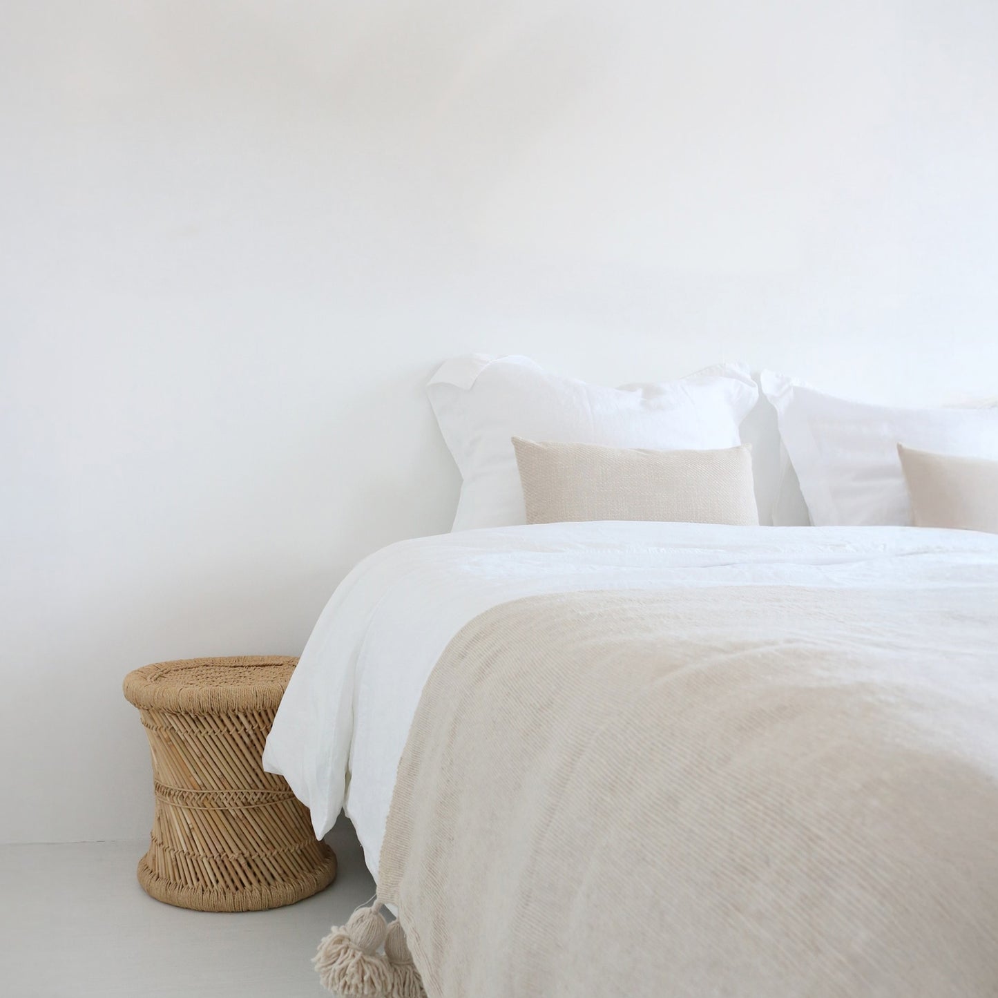 Neatly made bed with white bedding and beige blanket in a minimalistic room.