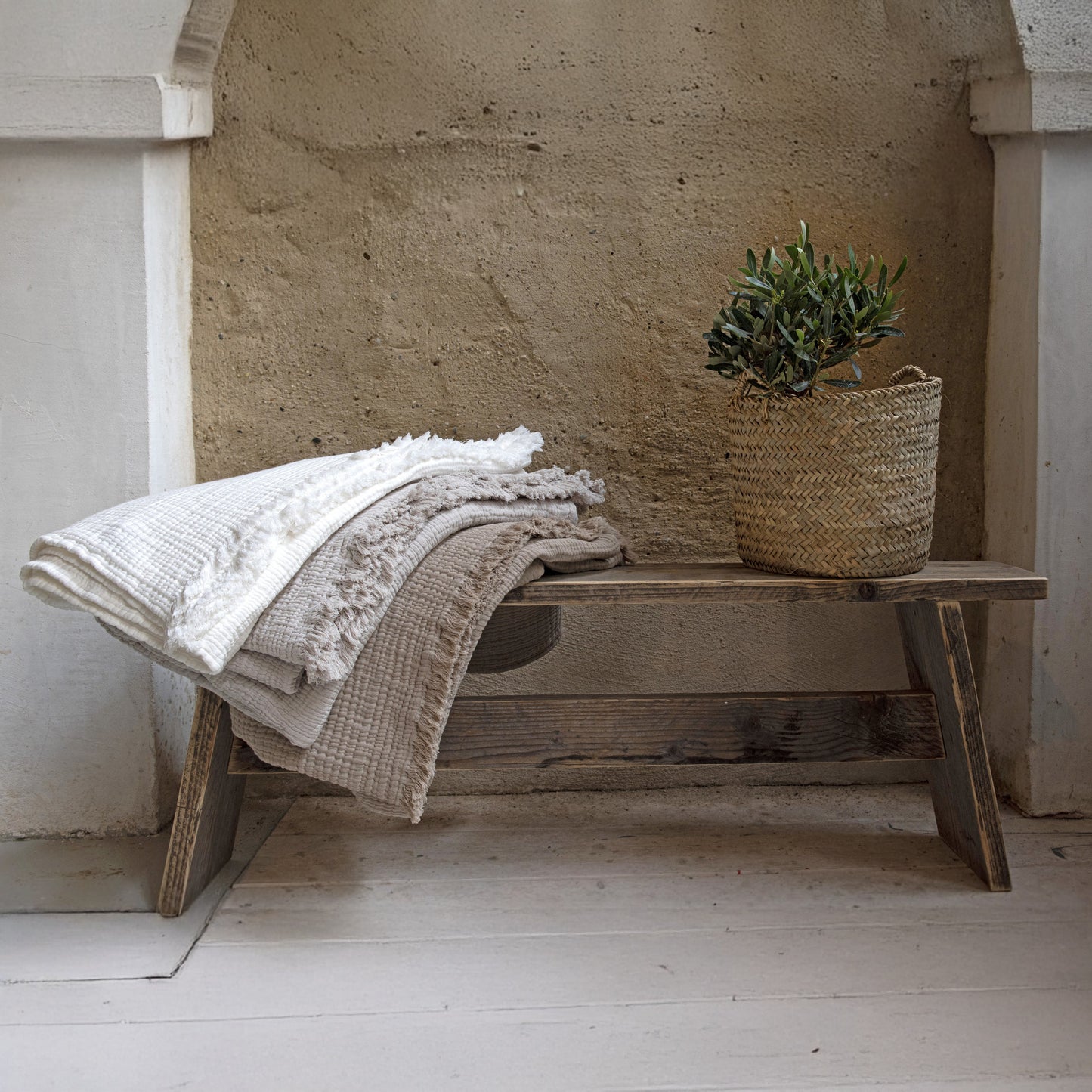 Wooden bench with a blanket and plant against a stone wall.